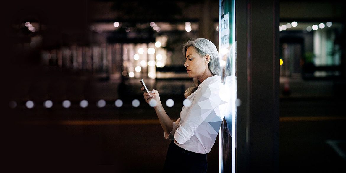 Eine Frau die ein Smartphone in der Hand hält und sich an einer Werbetafel anlehnt.