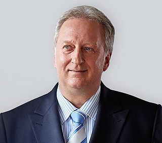 Ein Mann mit kurzen grauen Haaren, der einen blauen Anzug mit Krawatte trägt